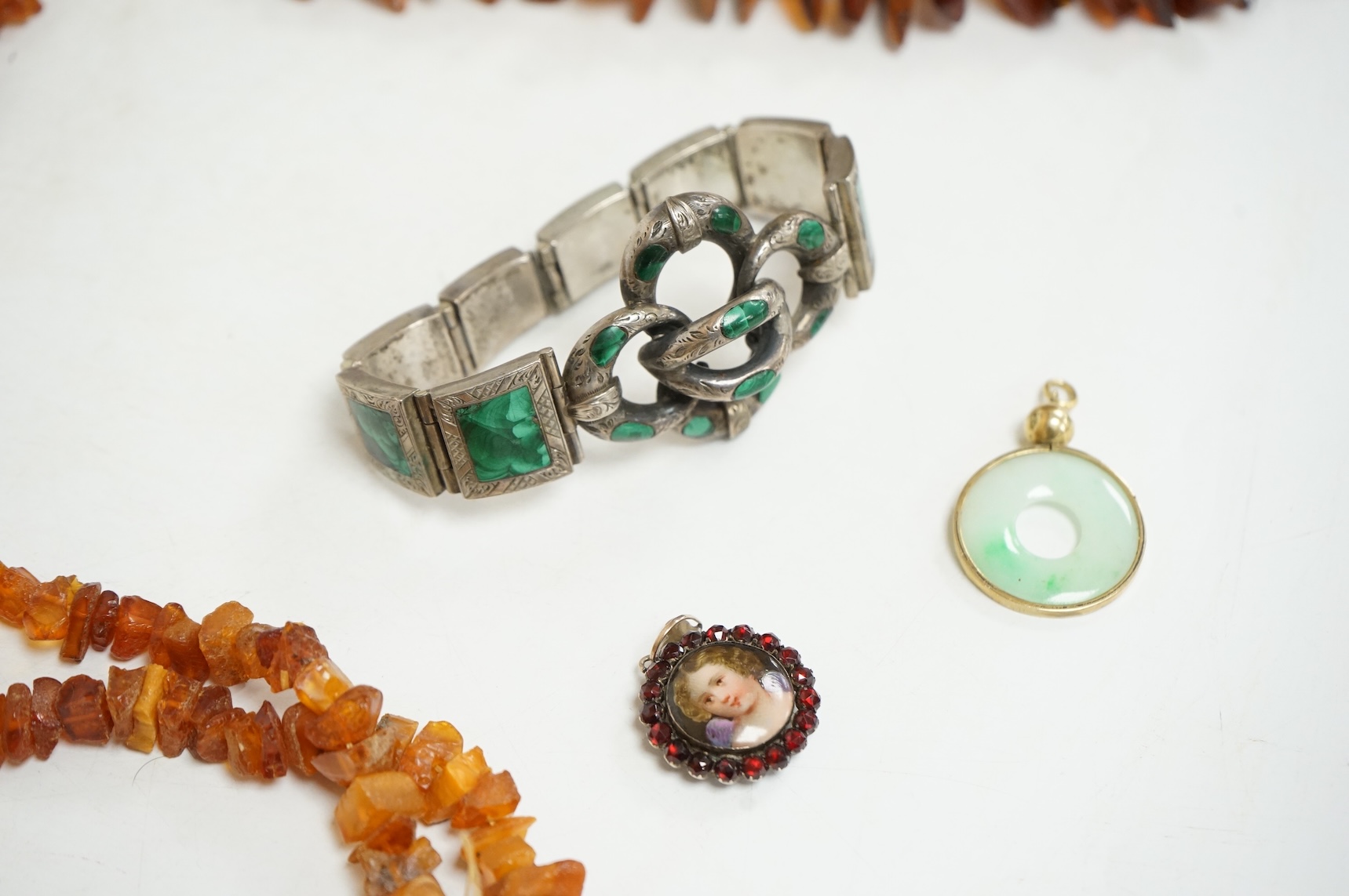 An early to mid 20th century engraved white metal and malachite set 'knot' bracelet, together with a Victorian garnet and enamel portrait pendant, a mounted jadeite disc pendant and two amber necklaces.